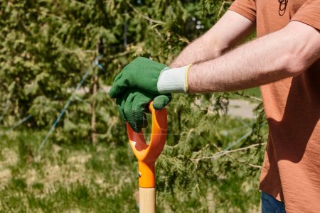 Téléchargez les photos : Vue recadrée de l'agriculteur dans des gants pelle d'exploitation tout en restant debout à l'extérieur, soins des plantes - en image libre de droit