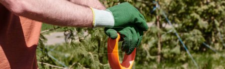 vista recortada del agricultor en guantes sosteniendo la pala mientras está parado al aire libre, pancarta de cuidado de plantas