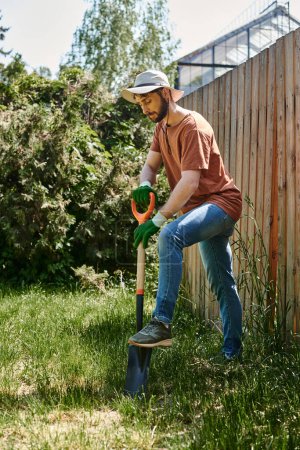 granjero de buen aspecto con barba que usa sombrero de sol y tierra de excavación con pala, cuidado de plantas