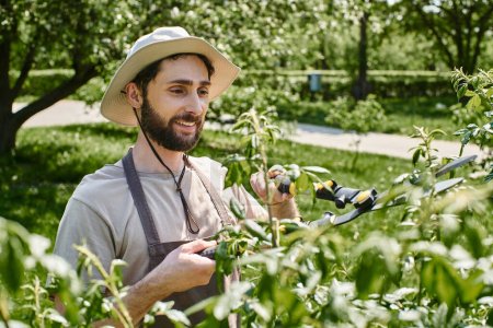 Téléchargez les photos : Heureux jardinier en chapeau de soleil taille brindilles d'arbre avec de gros ciseaux de jardinage et de travailler à l'extérieur - en image libre de droit