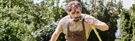 bärtiger Gärtner in Leinenschürze trinkt nach Gartenarbeit Wasser aus Schlauch, freimütiges Banner