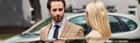 barbudo elegante hombre de negocios y mujer rubia mirándose el uno al otro cerca del coche en la calle, pancarta