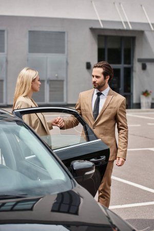 stylish bearded businessman and elegant woman holding hands near luxury car on city street