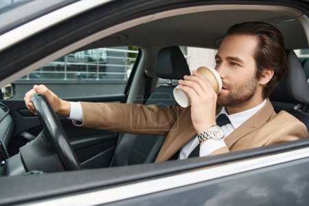 schöner bärtiger Geschäftsmann im beige eleganten Anzug, der Coffee to go trinkt und Auto auf der Straße fährt