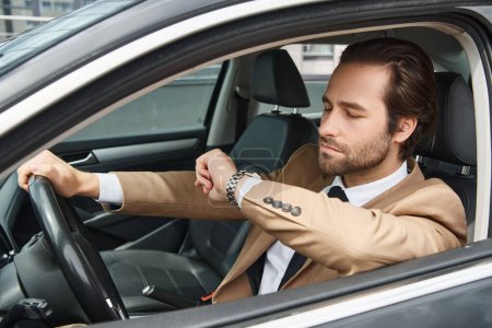 gutaussehender bärtiger Geschäftsmann in offizieller Kleidung, der auf die Armbanduhr schaut, während er Auto auf der Straße fährt