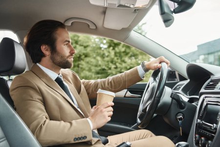 elegant bearded businessman in beige suit holding takeaway drink and driving car on urban street