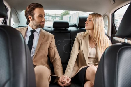 elegante pareja de negocios en el desgaste formal de la mano y buscando alfombra entre sí en el coche, atracción