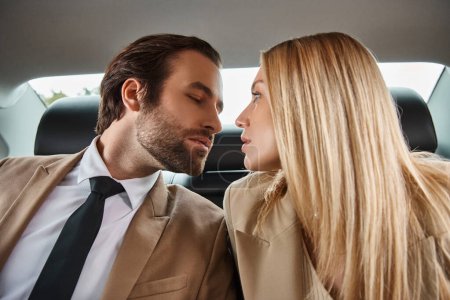 handsome businessman and attractive blonde woman sitting face to face in luxury car, seduction