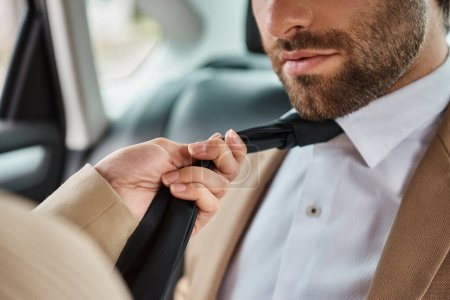 cropped view of passionate woman pulling tie on bearded business colleague and seducing him in car