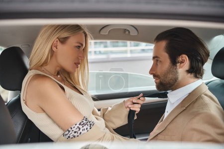 passionate blonde businesswoman pulling tie of handsome colleague seducing him in car, love affair