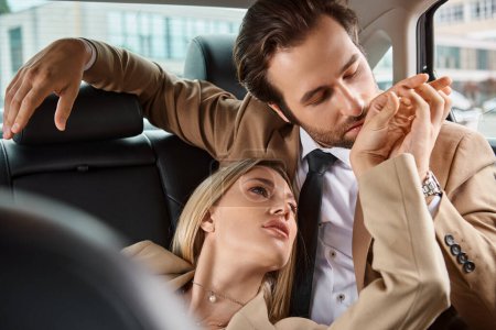 hombre de negocios en traje besar la mano de la mujer rubia apasionada mientras viaja en coche, romance