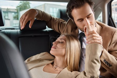 hombre de negocios en traje besar mano de mujer rubia apasionada mientras viaja en coche, seducción