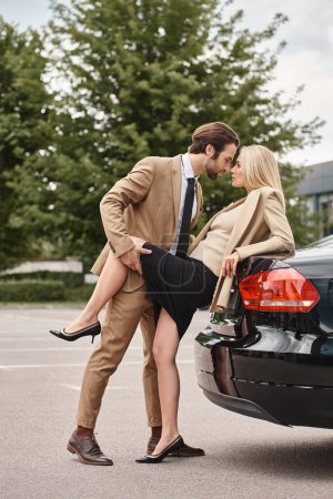 handsome man in formal wear seducing stylish blonde businesswoman near car on street, love affair