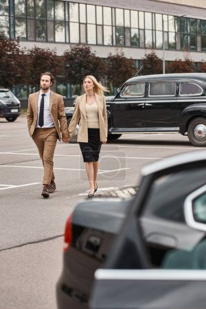 elegante pareja de negocios en formal desgaste cogido de la mano mientras camina a lo largo de aparcamiento, romance