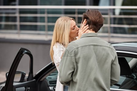 passionate and blonde woman and stylish man embracing near car on city street, urban romance