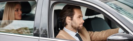 elegant confident man in formal wear driving car with attractive blonde businesswoman on rear seat
