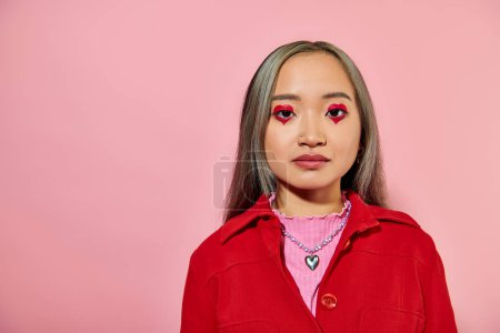 Porträt einer jungen Asiatin mit herzförmigem Augen-Make-up und gefärbten Haaren, die vor rosa Hintergrund posiert