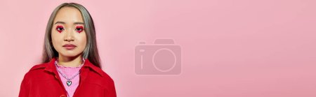 portrait of young asian woman with heart shaped eye makeup and dyed hair posing on pink, banner