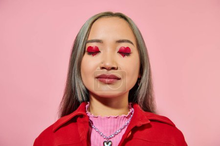 Téléchargez les photos : Portrait de jeune femme asiatique avec maquillage des yeux en forme de coeur et cheveux teints posant avec les yeux fermés - en image libre de droit