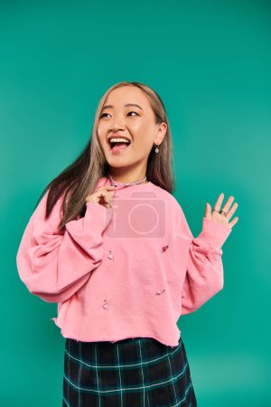 Foto de Retrato de mujer asiática excitada en sudadera rosa tirando de collar en forma de corazón sobre fondo azul - Imagen libre de derechos