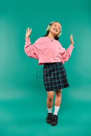 Foto de Longitud completa de positivo asiático chica en inalámbrico auriculares bailando en turquesa fondo - Imagen libre de derechos