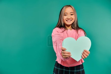14 february concept, cheerful asian woman holding heart shaped carton on turquoise background