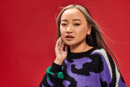 attractive and young asian woman with dyed hair in vibrant sweater with animal print posing on red