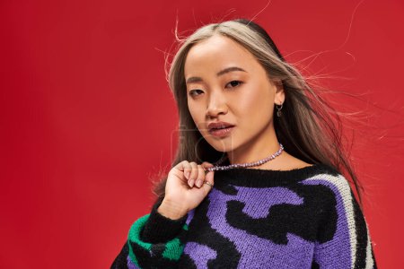 beautiful young asian woman with dyed hair in vibrant sweater with animal print touching necklace