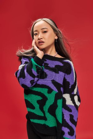 pretty young asian woman with dyed hair in sweater with animal print posing with hand near face