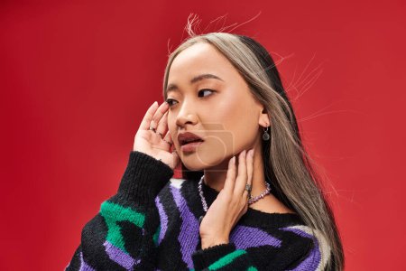 attractive young asian woman with dyed hair in sweater with animal print posing with hands near face