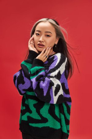 junge hübsche asiatische Frau mit gefärbten Haaren im Pullover mit Animal Print posiert mit händennahem Gesicht
