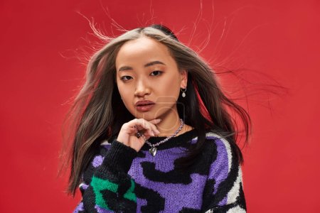 Wind weht im Gesicht der attraktiven jungen Asiatin mit gefärbten Haaren im Pullover mit Animal Print