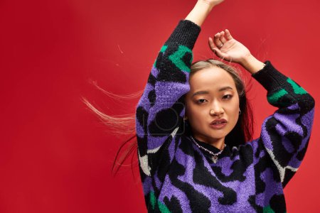 pretty young asian woman in vibrant sweater with animal print posing with raised hands on red