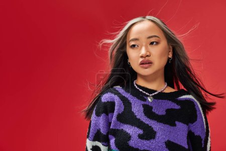 attractive young asian woman in vibrant sweater with animal print with heart shaped necklace on red