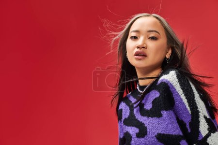 pretty young asian woman in vibrant sweater with animal print with heart shaped necklace on red