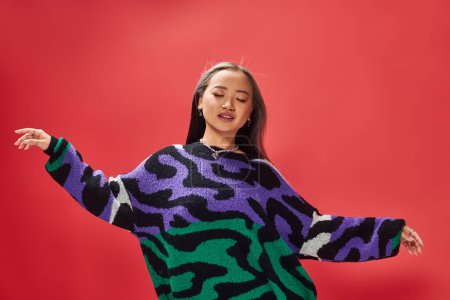 pretty young asian girl in vibrant sweater with animal print with heart shaped necklace on red, ease