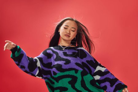 young asian girl in vibrant sweater with animal print with heart shaped necklace on red, ease
