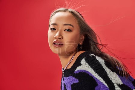 young asian girl in vibrant sweater with animal print with heart shaped necklace on red backdrop