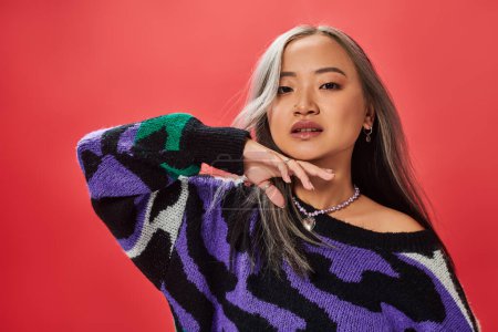 young asian girl in sweater with animal print with heart shaped necklace posing with hand near chin