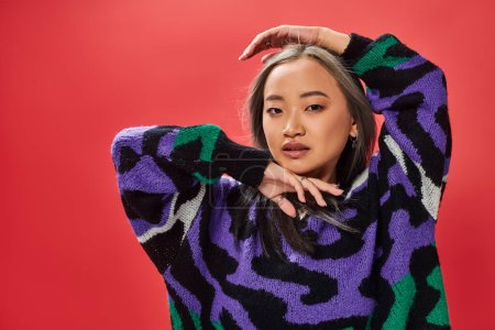 young asian girl in sweater with animal print with heart shaped necklace posing with hands near face