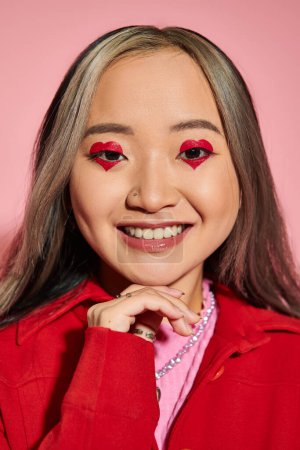 Téléchargez les photos : Concept de Saint-Valentin, heureuse femme asiatique avec maquillage des yeux en forme de coeur souriant sur fond rose - en image libre de droit
