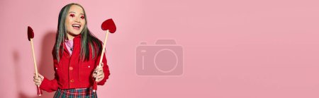 Valentinstag Banner, aufgeregt asiatische Amor Mädchen mit herzförmigen Augen Make-up hält Pfeile auf rosa