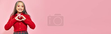 Téléchargez les photos : Bannière Saint-Valentin, heureuse fille asiatique avec maquillage des yeux rouges montrant coeur avec les mains sur rose - en image libre de droit