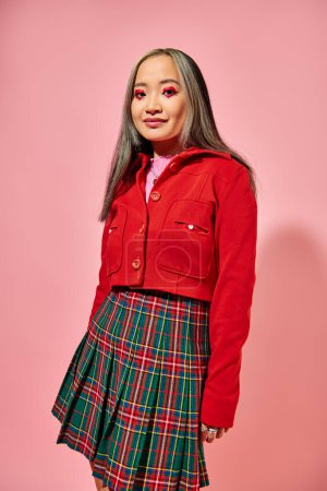 Valentines day, cheerful asian young woman with heart eye makeup posing in red jacket on pink