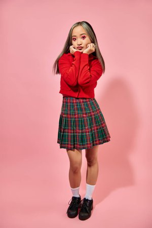 Valentines day, full length of asian young woman with heart eye makeup posing in red jacket on pink