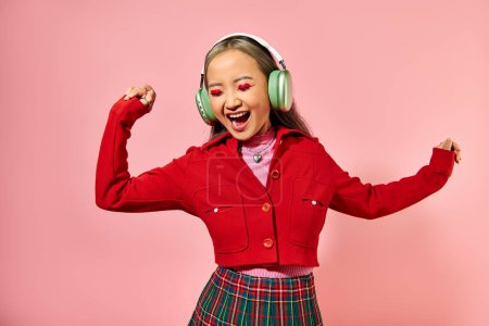 emocionado joven asiático mujer escuchar música en inalámbrico auriculares bailando en rosa telón de fondo