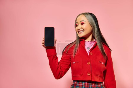 happy asian woman with red Valentines day makeup showing smartphone with blank screen on pink
