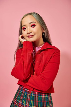 Foto de Retrato de lindo asiático joven mujer con corazón forma ojo maquillaje mirando cámara en rosa telón de fondo - Imagen libre de derechos