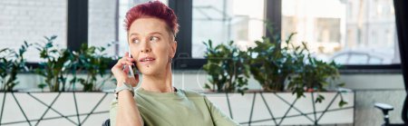 stylish queer manager talking on mobile phone and looking away in modern office, horizontal banner