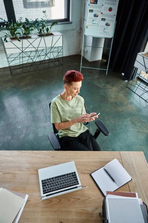 Photo for High angle view of queer manager messaging on smartphone near laptop and documents on work desk - Royalty Free Image